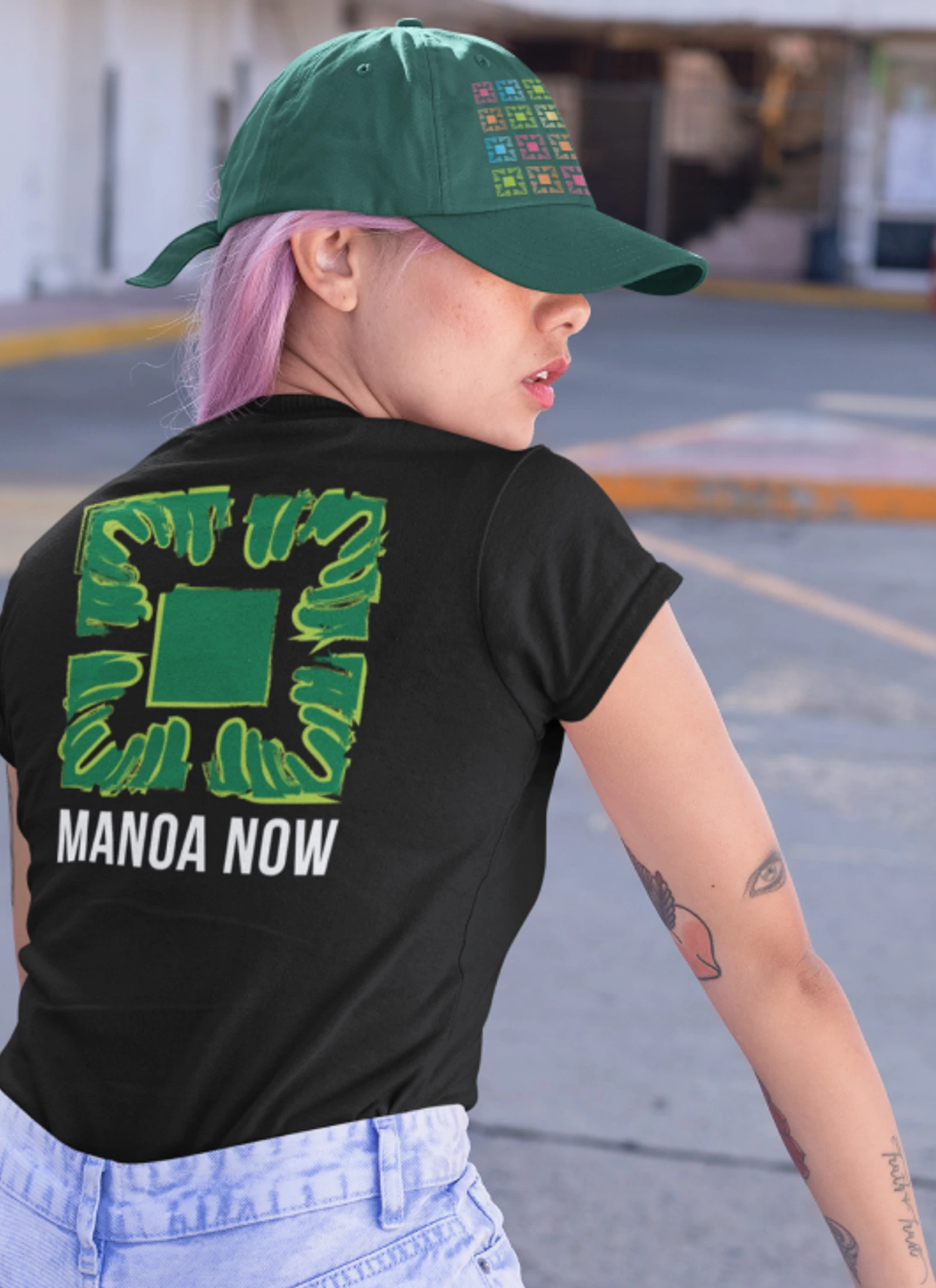 Model wearing a black Manoa Now shirt with a large green back graphic.