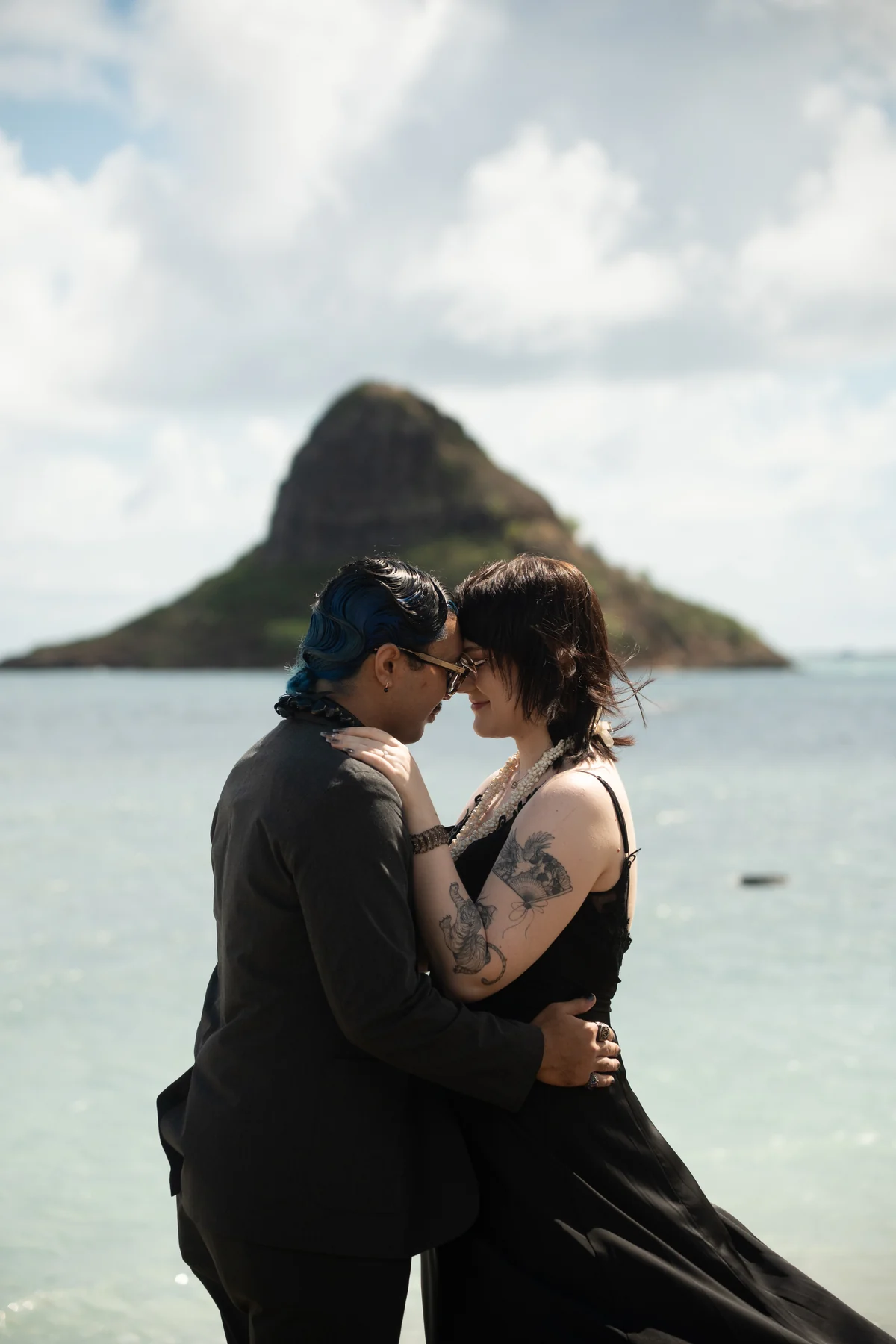 A couple embracing on a beach with an island in the distance.