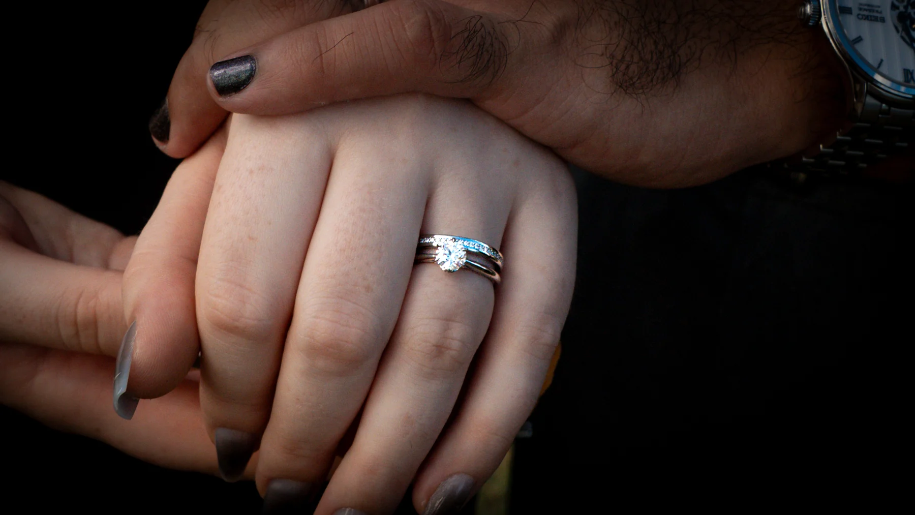 Close view of a wedding ring on a hand against a dark background.