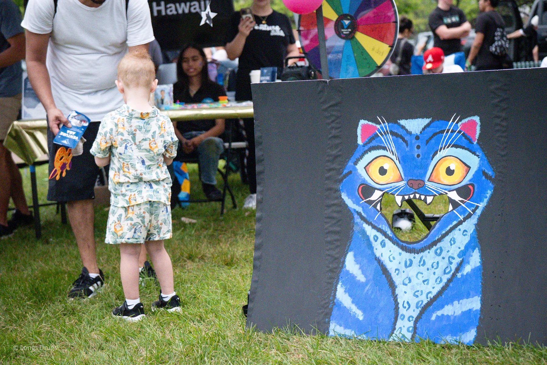A child standing beside a colorful cat painting at a community event.