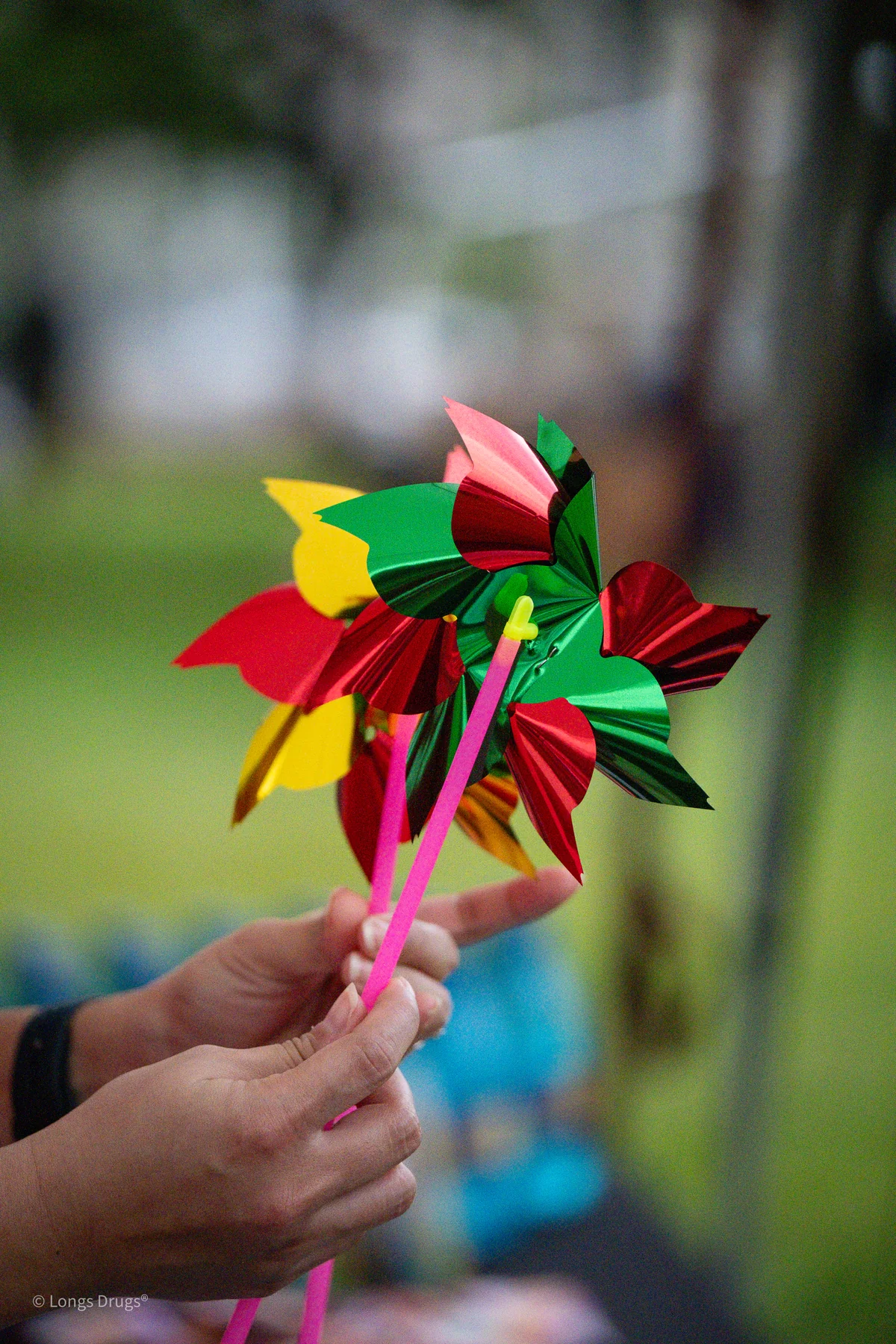 A hand holding a bright multicolored pinwheel against a soft green background.