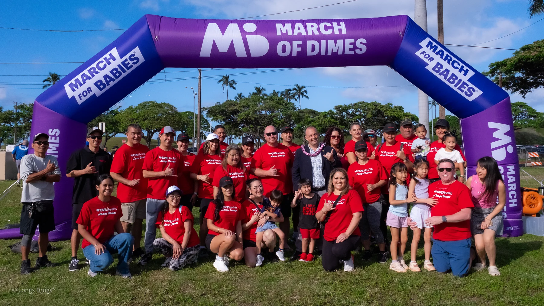 A large volunteer group gathered beneath a March of Dimes event arch.