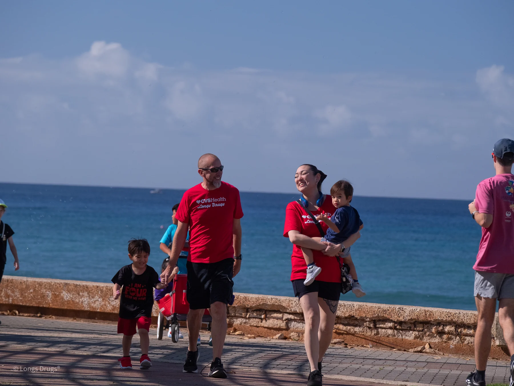 Families walking along a coastal route with the blue ocean behind them.