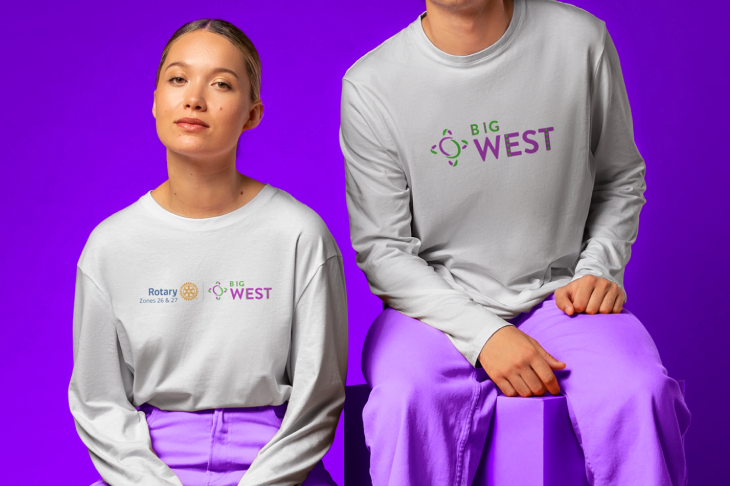 Two models seated in Big West apparel against a purple studio background.